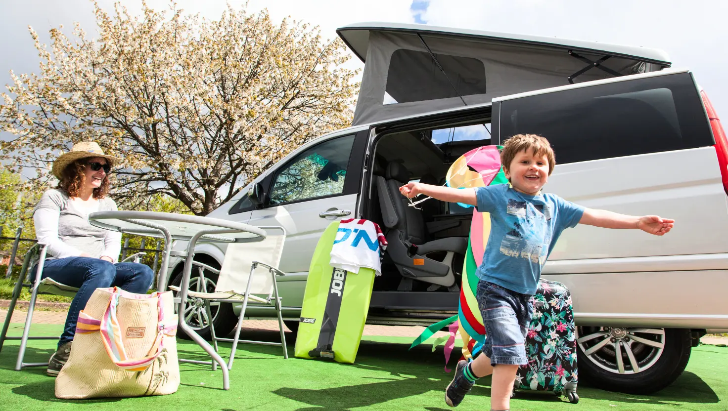 mum sat at a picnic table and young boy running, by their white campervan at one of the UK campervan picnic spots