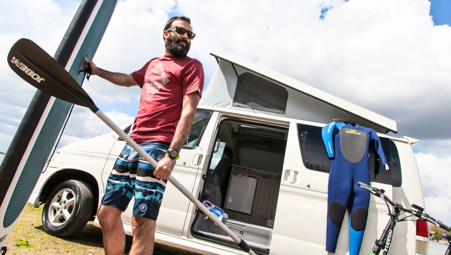 white Free Spirit Campervan with a man holding a surf board for surfing campervan trips UK