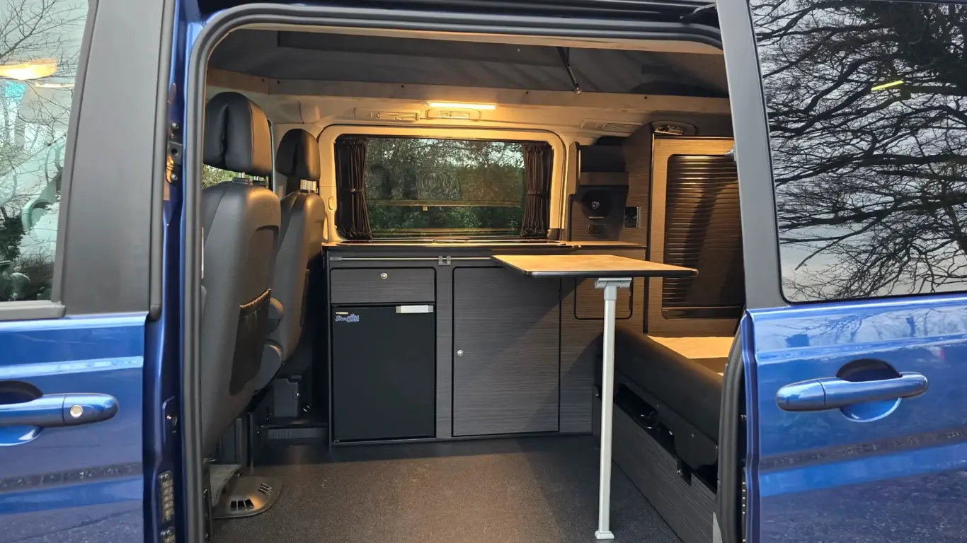 inside a blue compact campervan, showing the table, kitchenette and seating