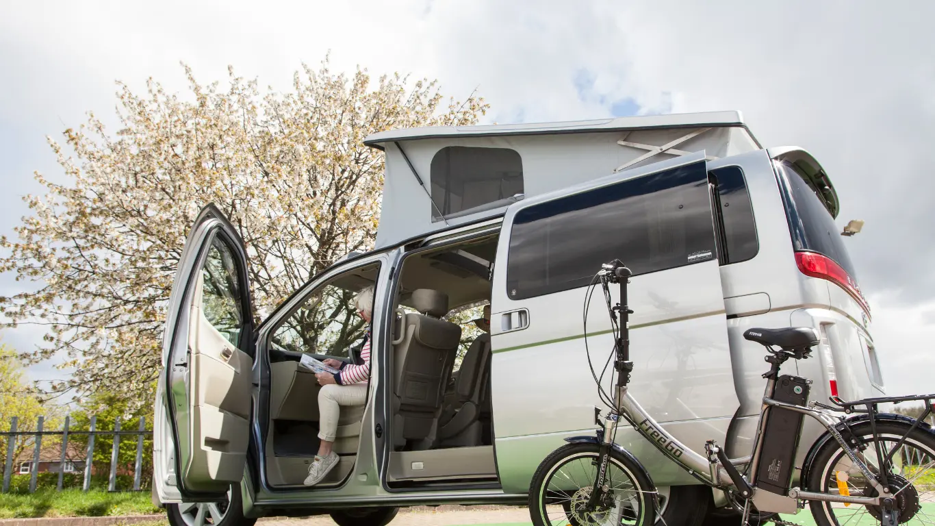 silver Campervan for Bikes with a woman siting reading in the van with a bike leaning against the campervan